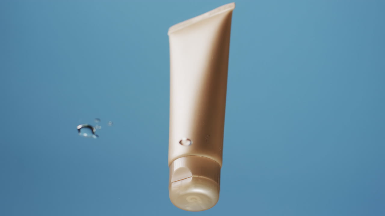 video de un tubo de producto de belleza en el agua con espacio de copia en fondo azul