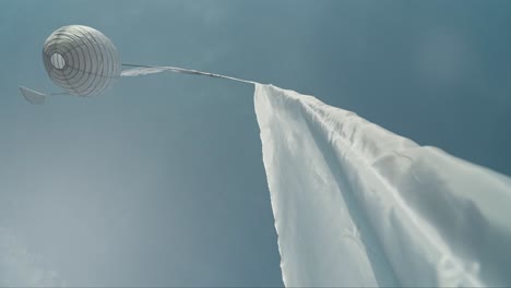 Balinese-white-latern-flag-swaying-in-light-breeze-on-sunny-day,-looking-up