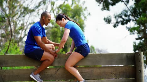 entrenador masculino ayudando a una mujer en forma a escalar una pared de madera durante una carrera de obstáculos de 4k