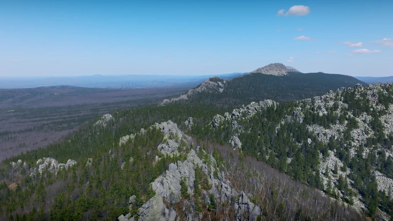 Ampio panorama aereo di una cresta montuosa rocciosa e di una fitta foresta di taiga sotto un cielo azzurro limpido nel Parco Nazionale di Taganay, Oblast di Chelyabinsk, Russia
