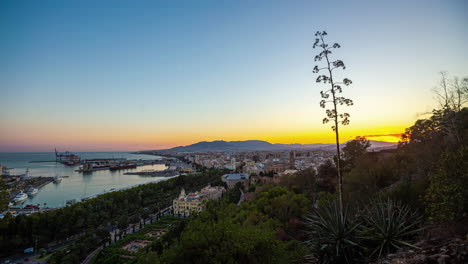 Timelapse-Overlooking-Puerto-de-Málaga,-Capturing-the-City's-Sunset-with-the-Moon-Setting-Over-the-Horizon