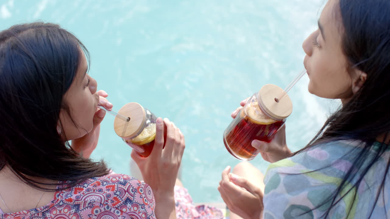 Drinking iced tea from mason jars, two teenage girls hanging out by pool