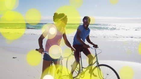 yellow bokeh animation over couple riding bicycles on beach