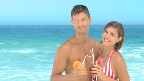 pareja posando con cócteles en una playa