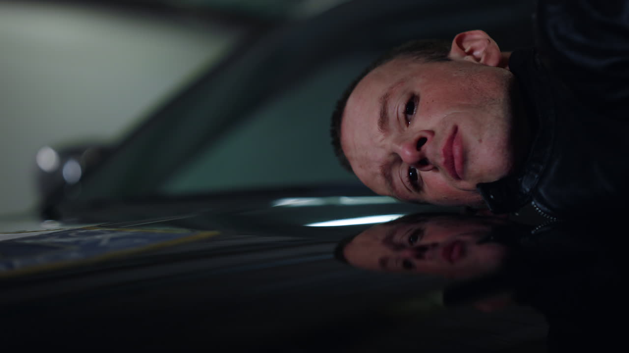 Verärgerter männlicher Krimineller liegt auf dem Kofferraum des Polizeiautos. Traurig verhafteter Mann posiert vor der Kamera.