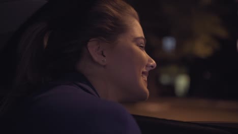 happy beautiful girl riding in a taxi at night sitting on the backseat and looking from the window at the night city life. happy