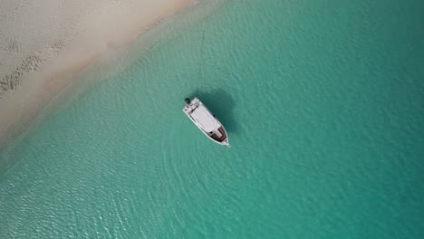 top-down view of white boat floating in clear blue caribbean water near white sand beach of madrisqui island, los roques, venezuela