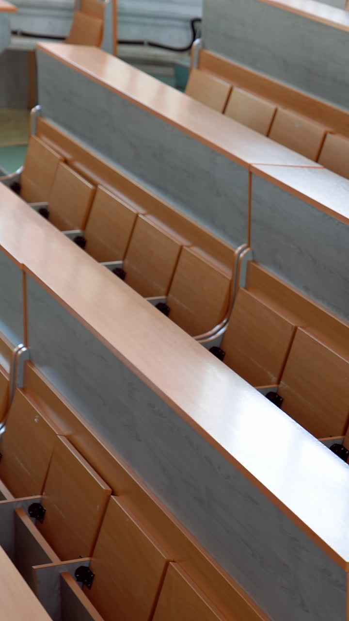 Modern desks in lecture hall. Rows of long wooden tables with vacant seats in the light auditorium at university. Classroom without students. Vertical video