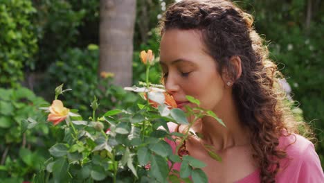 portrait of happy biracial woman smelling roses in garden