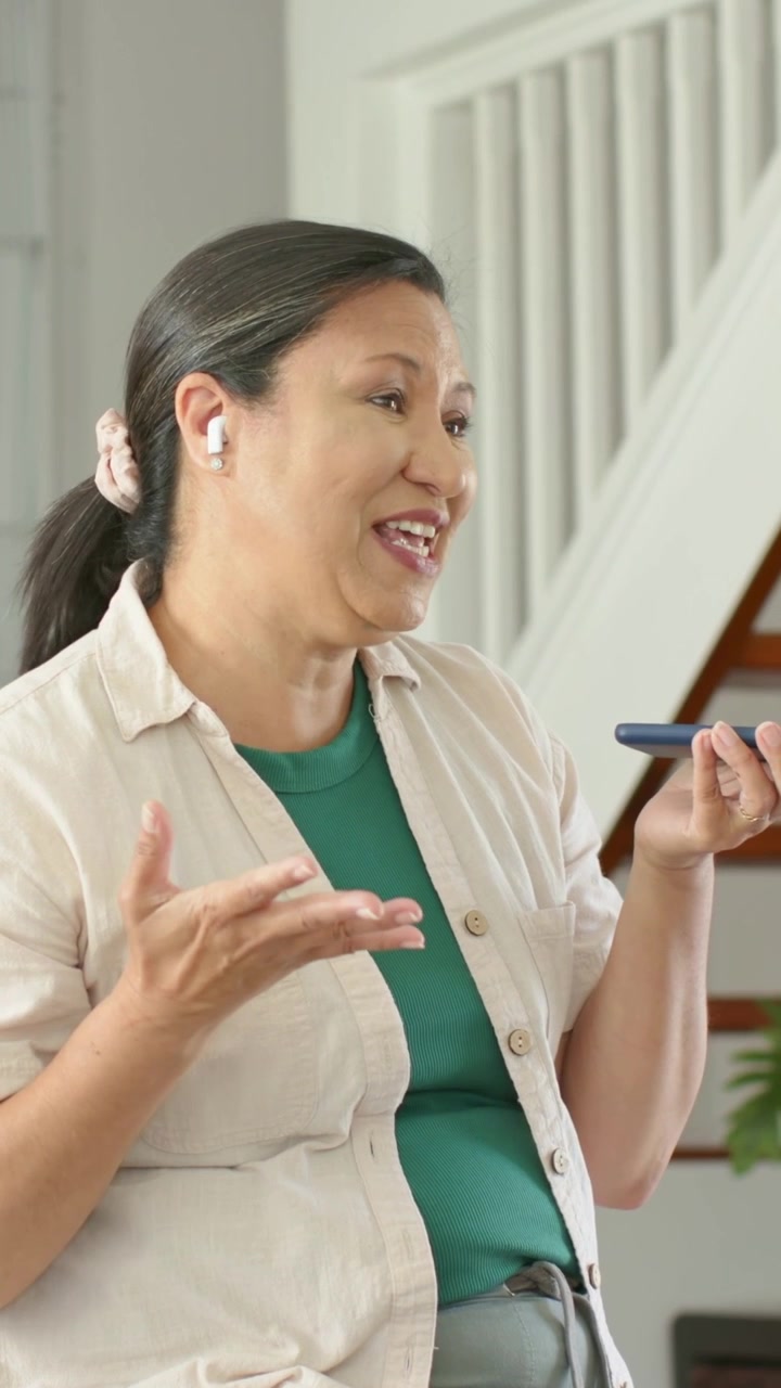 Video verticale: Ricevendo una chiamata, donna con maglietta verde che tiene il telefono e parla vicino alle scale con auricolari