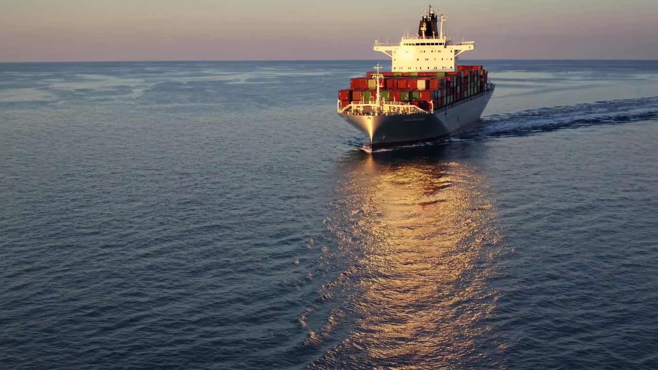 Aerial video of a cargo ship at sea during sunset, capturing a serene and expansive view