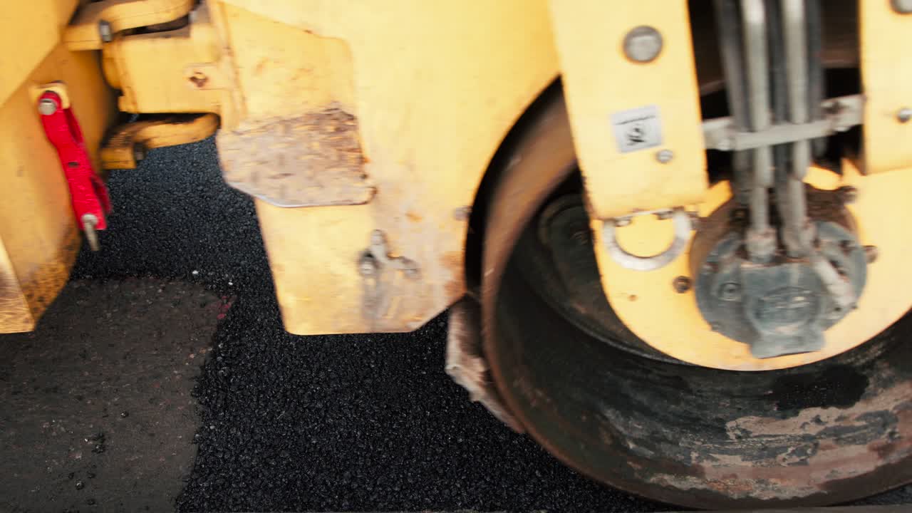 Huge compactor is driving over newly poured asphalt to compress it on top of the road