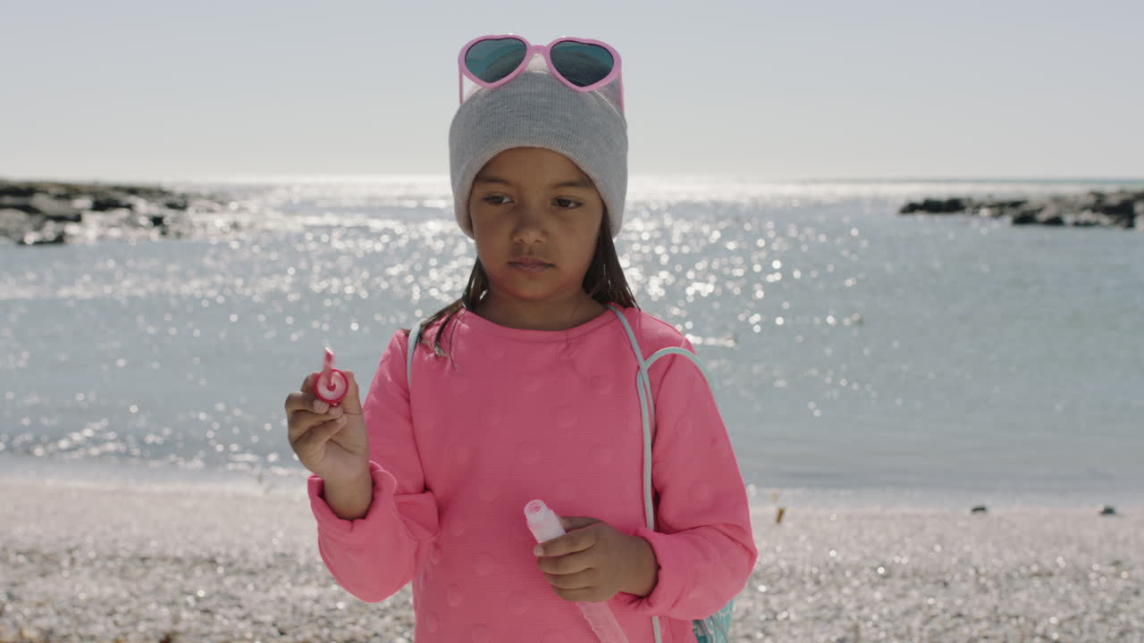 retrato de una niña soplando burbujas en la playa con ropa rosa