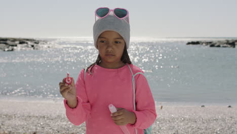 portrait of little girl blowing bubbles on beach wearing pink clothes