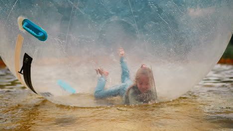 funny girl jumps and falls inside large water globe in pool