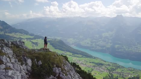 droneshot around a young asian woman who stands on top of a mountain in switzerland