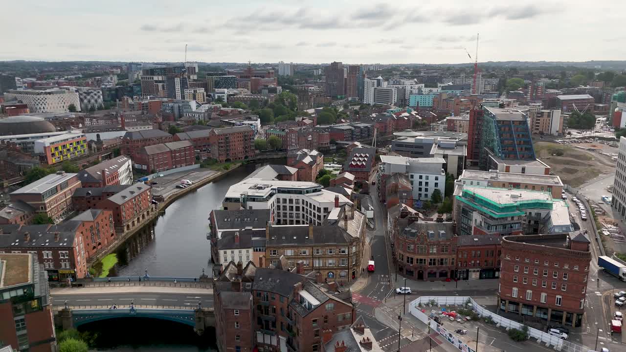 Drone camera glides above a contemporary business district with green spaces, modern buildings, and a river, under overcast daylight. Smooth forward movement reveals city layout