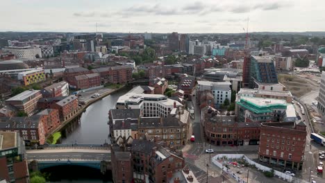 drone camera glides above a contemporary business district with green spaces, modern buildings, and a river, under overcast daylight. smooth forward movement reveals city layout