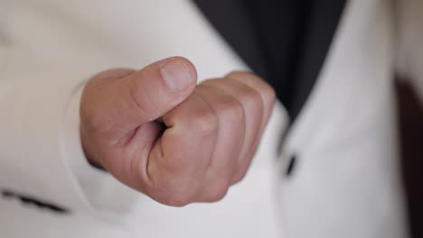 groom in gray jacket holding wedding rings on palm of his hand, man clenched rings in his fist