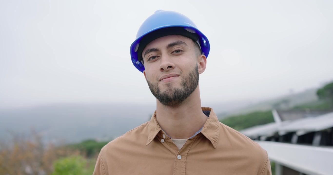 Uomo afroamericano tecnico che abbassa un pannello solare sul tetto mentre la telecamera si avvicina, notando l'obiettivo, con casco di sicurezza.