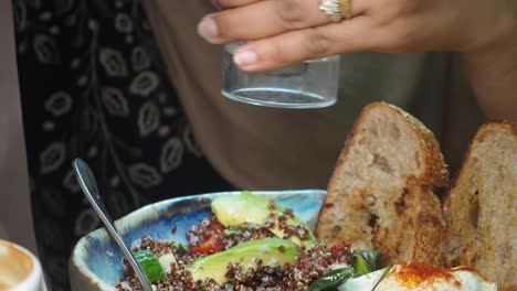 woman seasoning a quinoa bowl with toasted bread and eggs