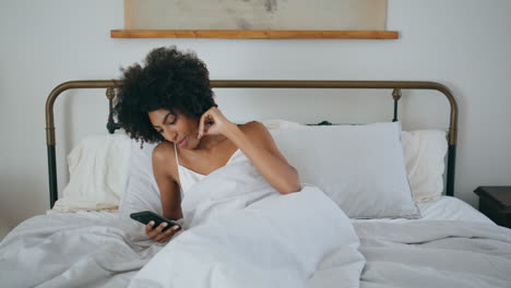 awaking girl yawning bed at morning. african woman reading phone laying pillow