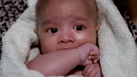 funny adorable two month old baby boy wrapped in towel sucking arm