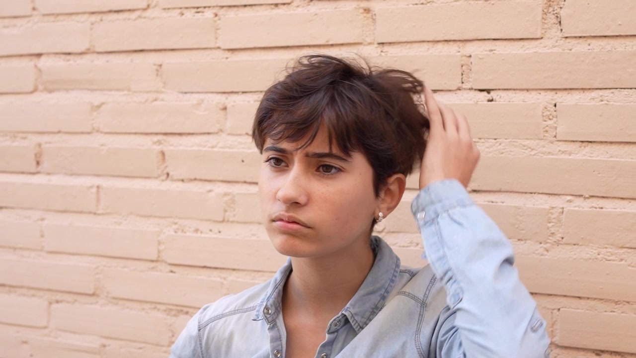 Una giovane donna pensierosa è in posa contro un muro di mattoni a vista all'aperto.