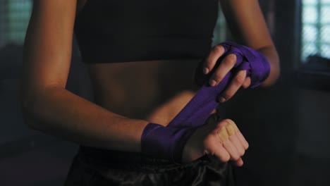 Closeup-view-of-muay-thai-female-boxer-wrapping-bandages-on-her-hands-before-fight-in-dark-room-with-smoke.-Shot-in-4k