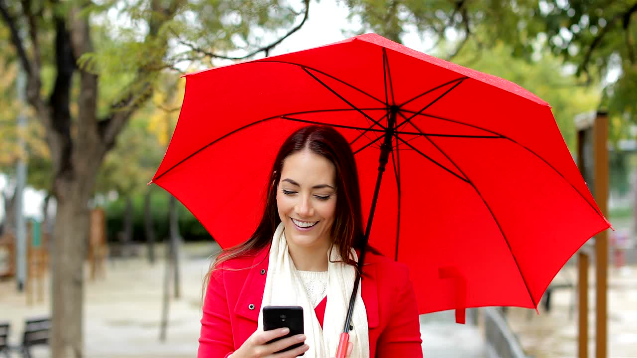 mujer feliz de rojo comprobando el teléfono bajo la lluvia