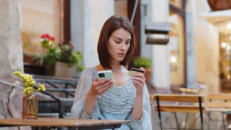 Young-woman-using-credit-bank-card-smartphone-while-transferring-money-order-food-in-cafeteria