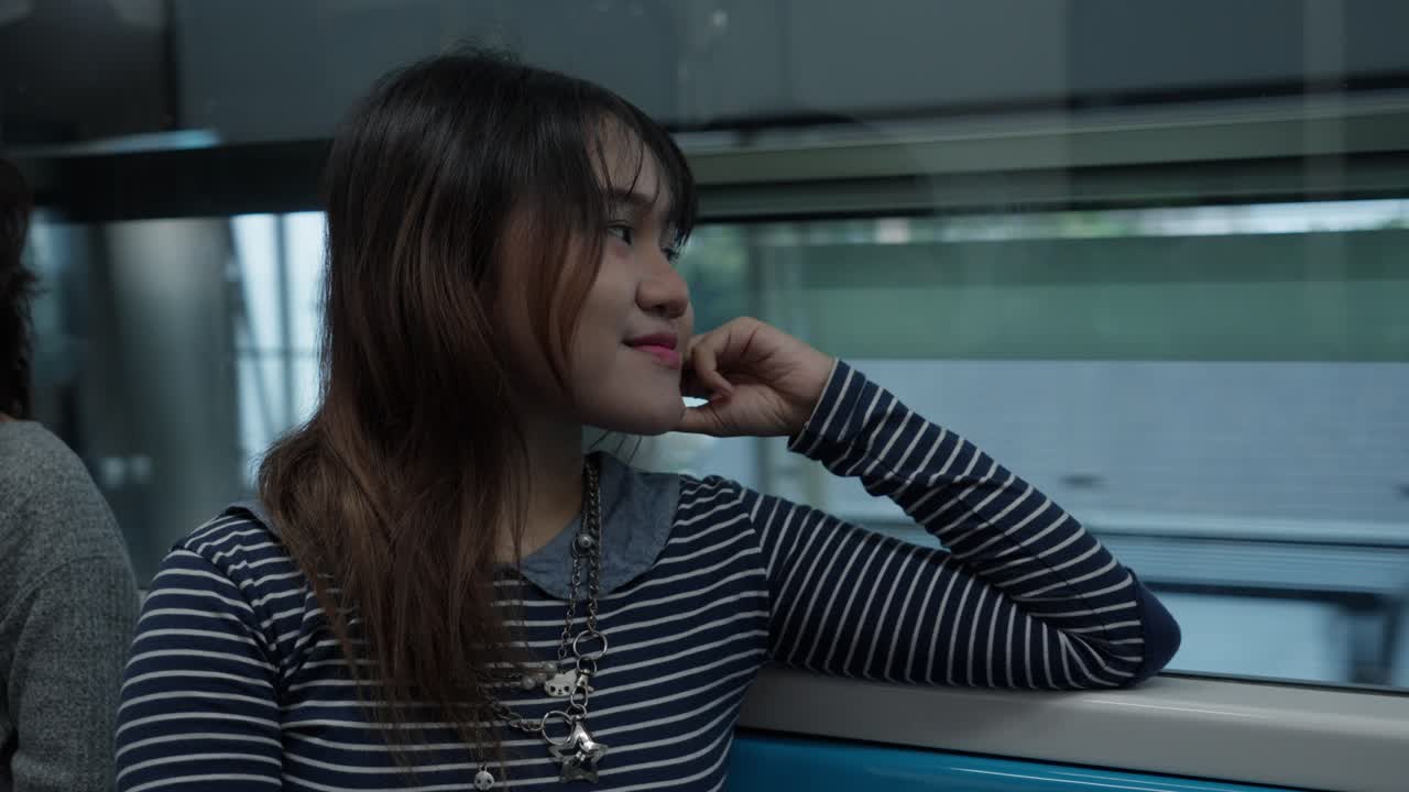 Young woman on a train gazes out the window with a thoughtful expression