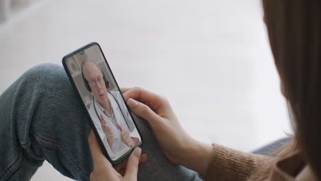 Woman-checks-possible-symptoms-with-professional-physician-using-online-video-chat.-Young-girl-sick-at-home-using-smartphone-to-talk-to-her-doctor-via-video-conference-medical-app.