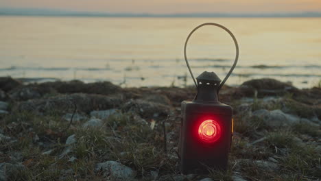 old-fashioned lantern illuminated with red light on lakeshore at sunset