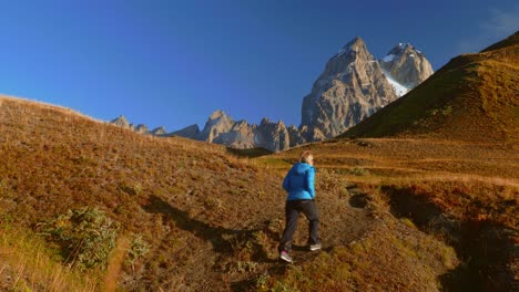 Tourist-in-Guli-pass-walking-towards-Mt-Ushba-on-sunny-morning,-Caucasus,-Georgia