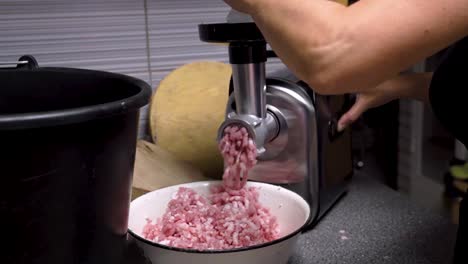 butcher grinding minced meat in grinder appliance in clean hygienic kitchen, close up