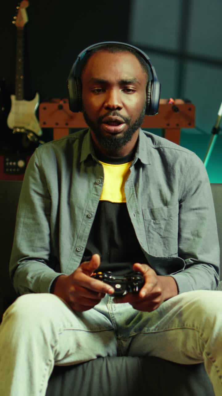 Vídeo vertical de um gamer no sofá usando controle e fones de ouvido para jogar videogame em casa