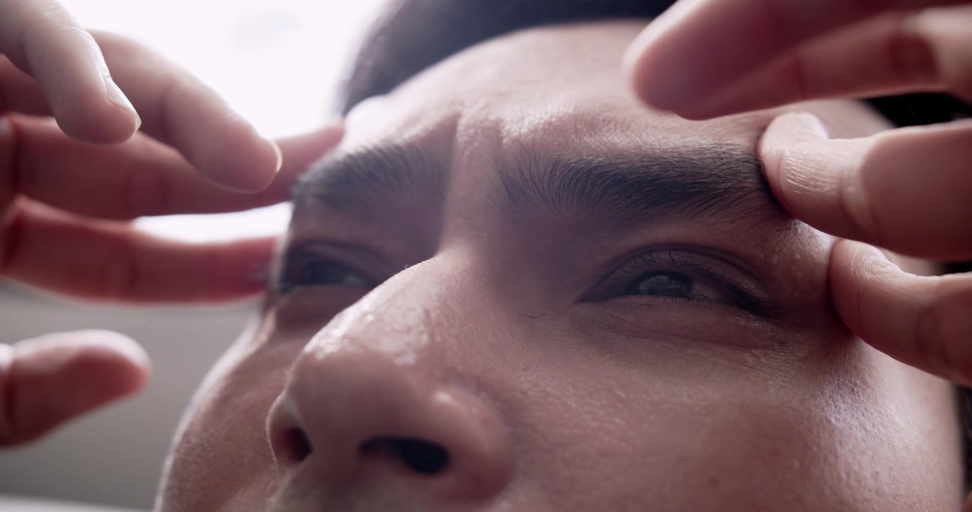 Jovem estressado sentado no sofá, recostado e massageando as têmporas e as sobrancelhas. Esta cena capta a tensão emocional e os desafios da vida moderna.