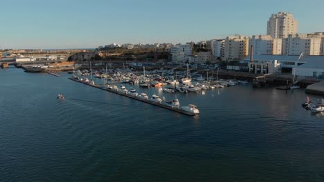 Aerial-of-moored-boats-at-Portimao-marina,-Algarve,-Portugal,-skyline-and-boat-coming