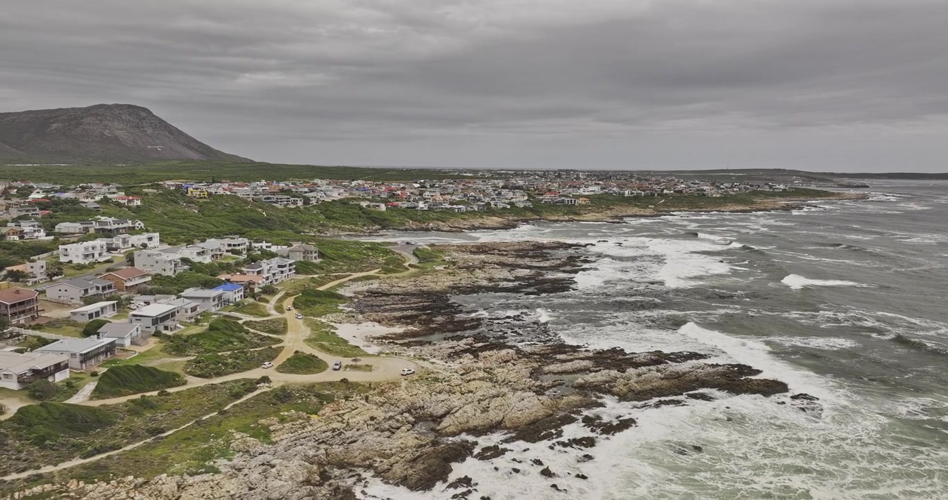 Gansbaai, Etelä-Afrikka, ilmakuva v3 ylilento De Keldersin ja Stanford's Coven kotien ympärillä kallioista rannikkoa pitkin vuorten ja pilvisten taivaiden alla – Kuvattu Mavic 3 Pro Cine -kameralla – 7. tammikuuta 2024.