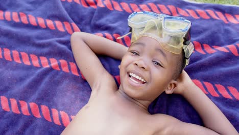 Porträt-Eines-Glücklichen-Afroamerikanischen-Jungen-Mit-Taucherbrille,-Der-Auf-Einem-Handtuch-Liegt