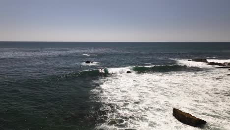 Surfer-in-Laguna-Beach-riding-a-wave-in-the-Pacific-Ocean-with-some-rocks,-blue-sky-and-no-clouds