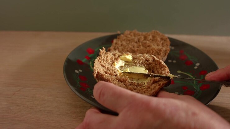 Hand buttering brown wholemeal bread for sandwich close up zoom slow motion shot selective focus