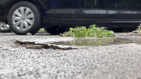 raindrops falling on the ground with parked car in background