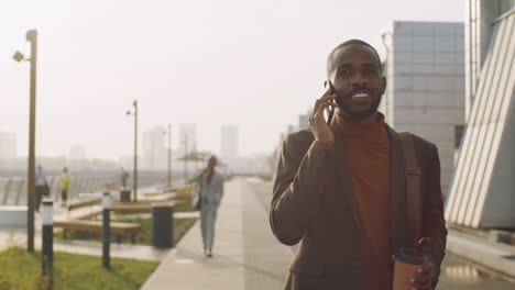 black businessman walking with coffee outdoor and talking on phone