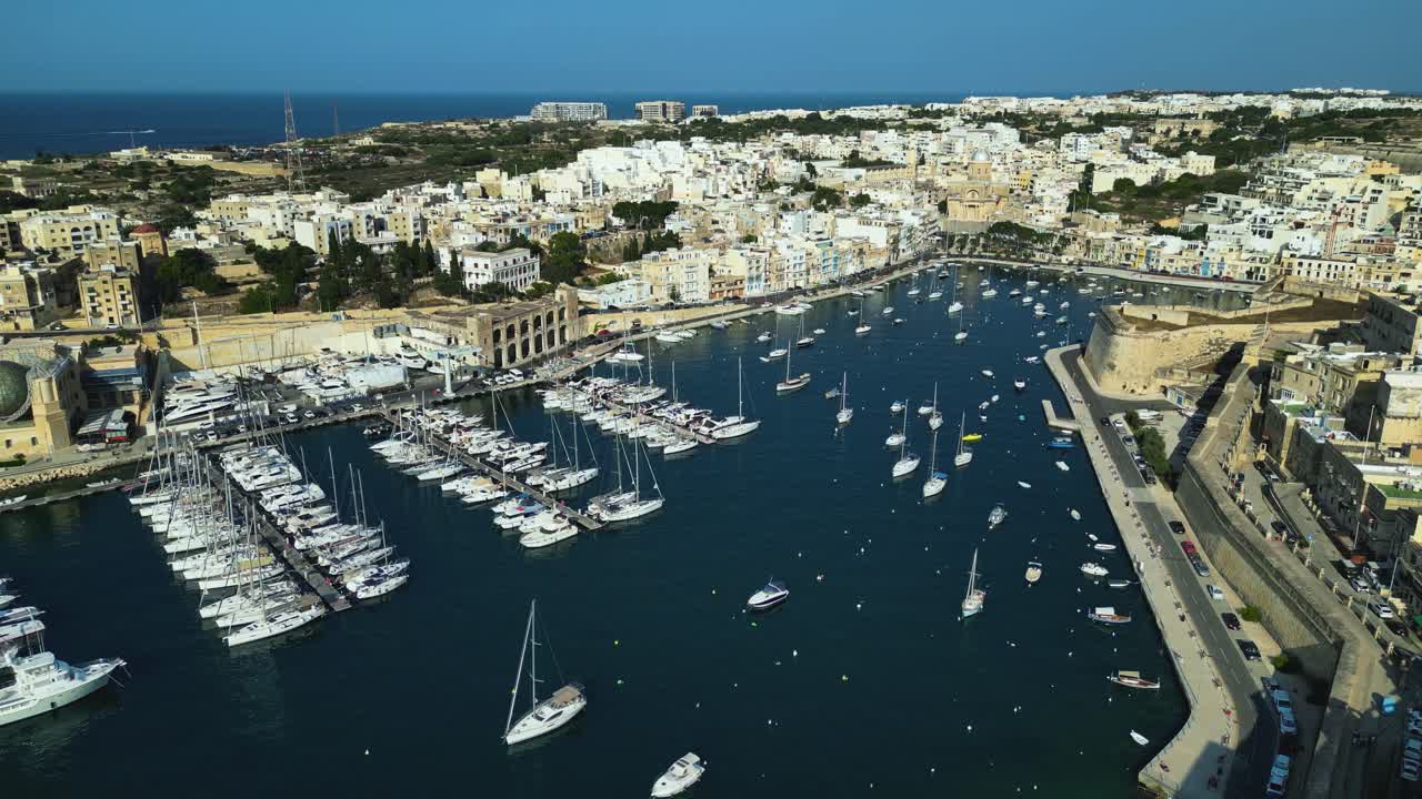 Drönare som etablerar en åkning av Birgus hamn med båtar, bryggor, stenbyggnader och klart blått kustvatten, Malta
