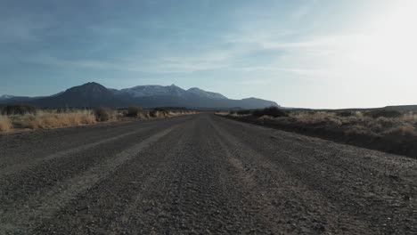 Aerial-view-of-Utah-desert-vastness-following-the-dirt-road-with-mountains-in-background,-USA