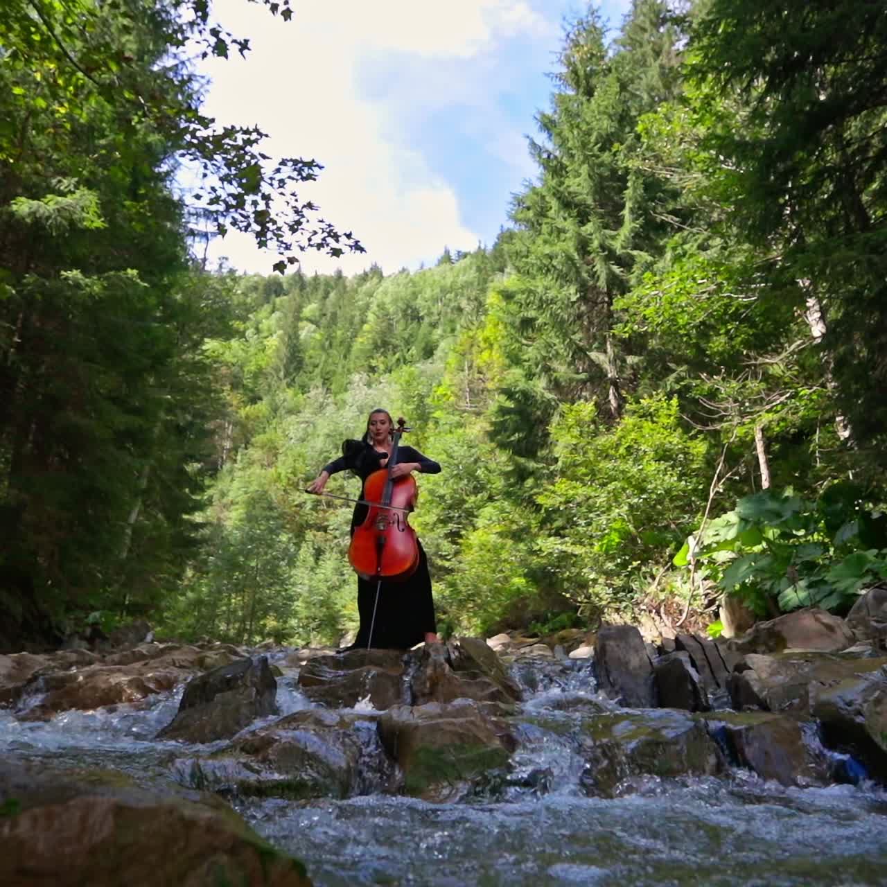 Pretty woman playing on a cello in nature. Huge cello in woman`s hands in the forest