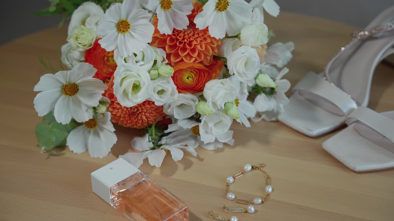 Elegant bridal setup featuring a fragrant perfume, pearl jewelry, and a vibrant floral bouquet. Perfectly lit and composed close-up shot capturing wedding day essentials
