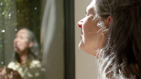 caucasian mature woman looking out window, reflecting